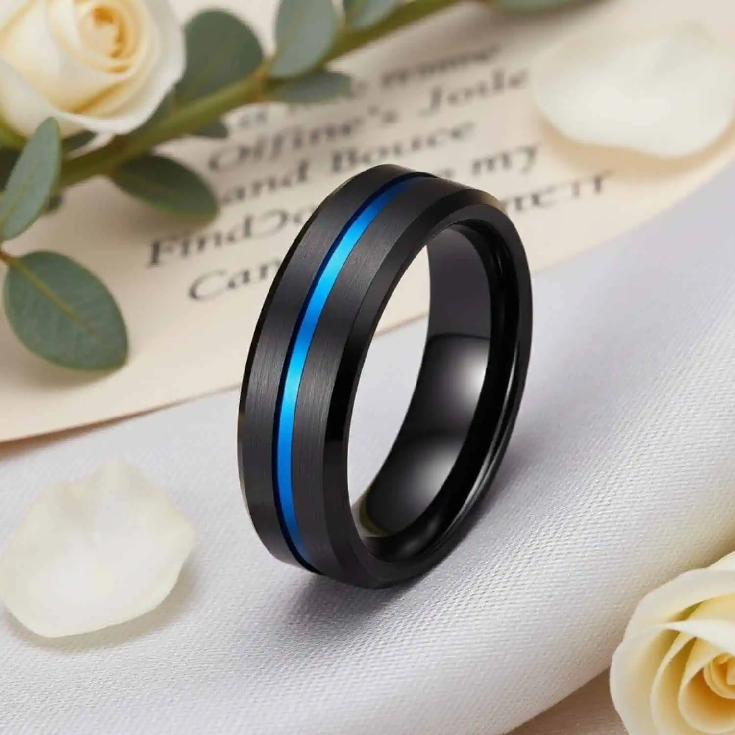 The Visionary black wedding band for men standing beside white flower petals and a handwritten note, with elegant white wedding flowers in the background.