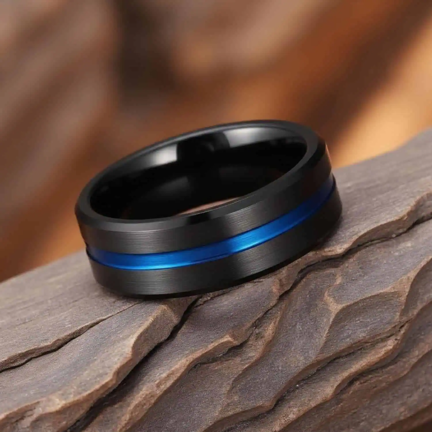 Close-up of the Visionary brushed black tungsten ring resting on a natural rock, showing the polished blue groove and polished bevelled edges in fine detail.