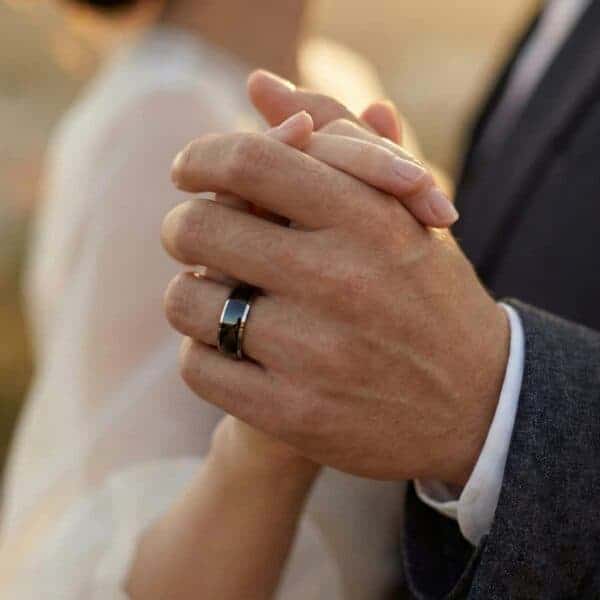At the wedding ceremony, the couple join hands ready to dance together. On the mans hand is his new wedding band - a black tungsten ring with silver edges.