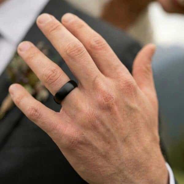 A close up of a mans hand wearing his brand new wedding ring. It is a black tungsten band with blue on the interior.