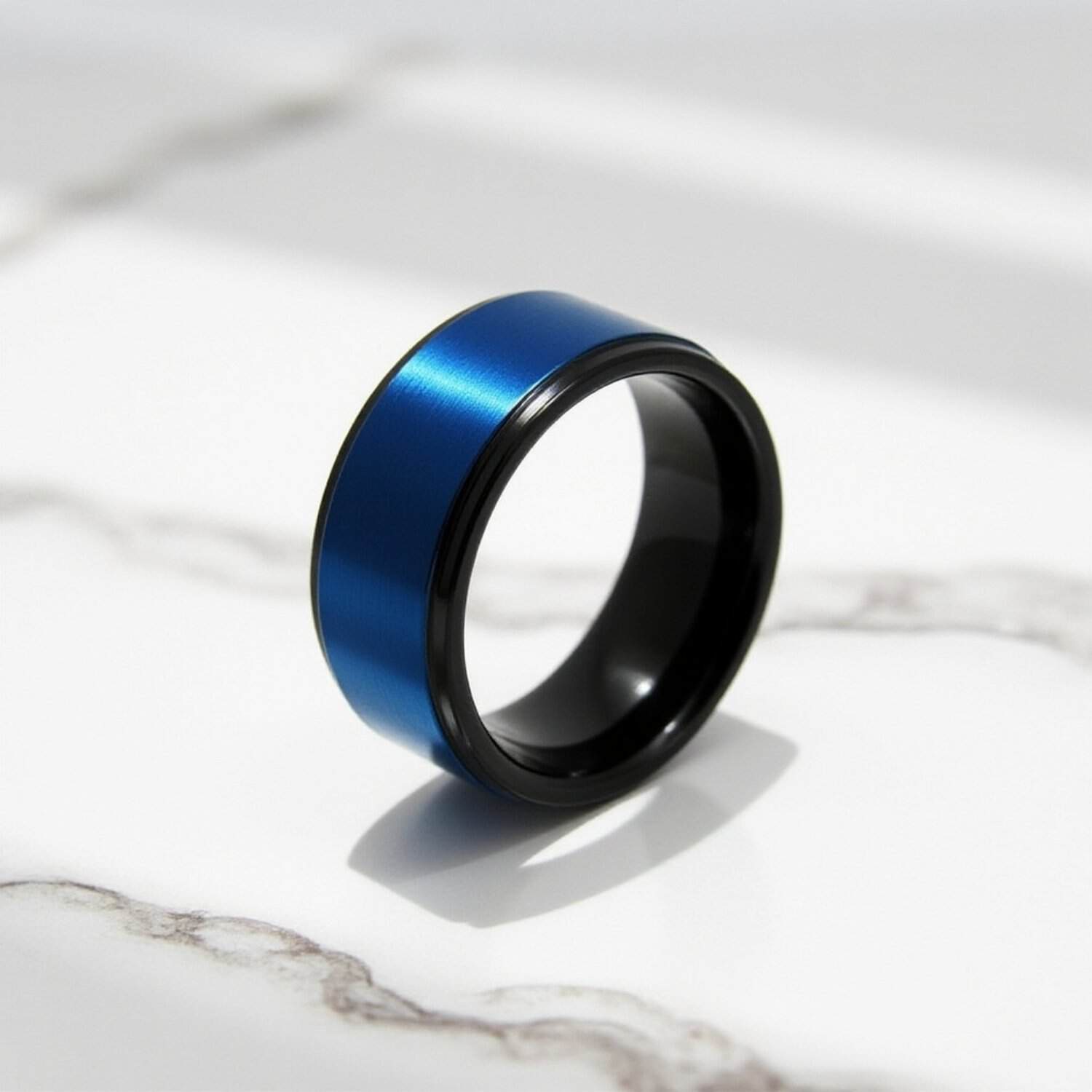 Close up of black tungsten ring with blue centre on white marble. surface.