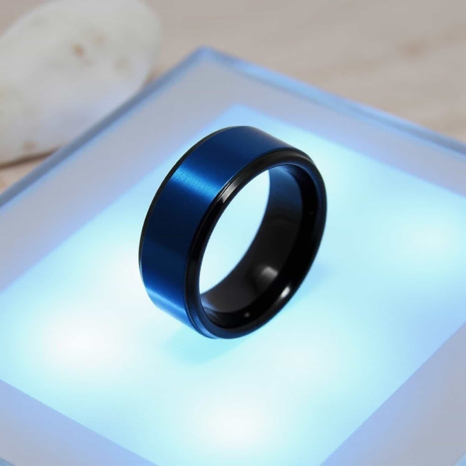 Close up detail of mens black tungsten ring with blue centre on light surface.