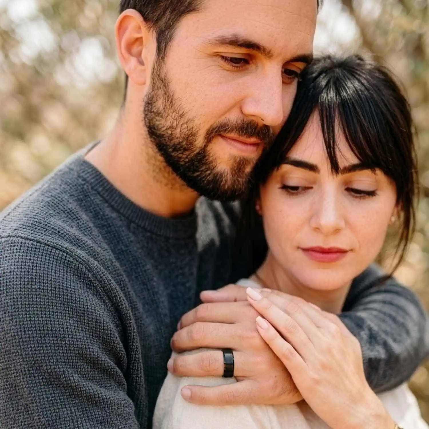 Couple embracing outdoors with trees in background, man wearing brushed black tungsten ring with polished edges