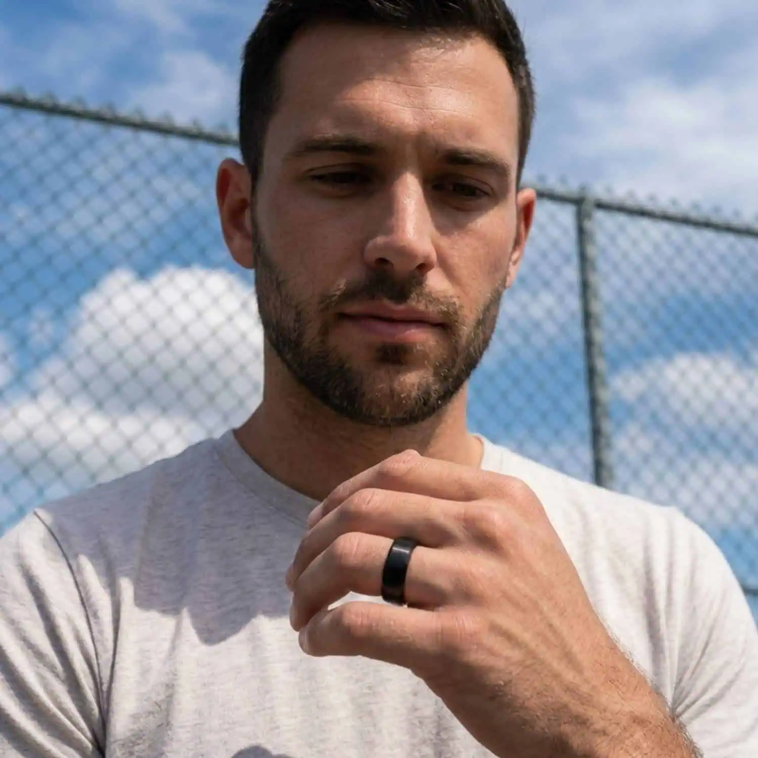Man facing camera with hand raised wearing brushed black tungsten ring with polished edges