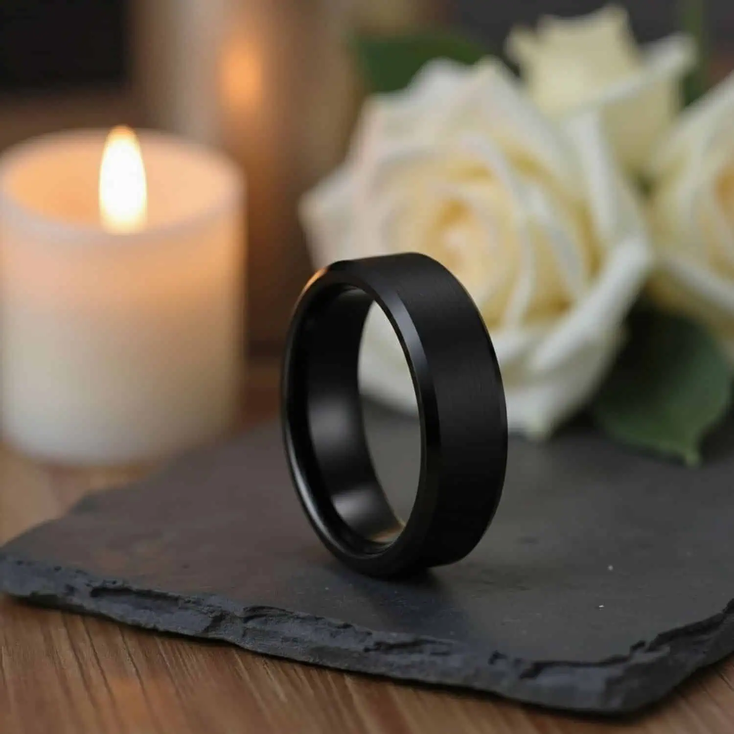 Brushed black tungsten ring with polished edges on slate with candle and white roses