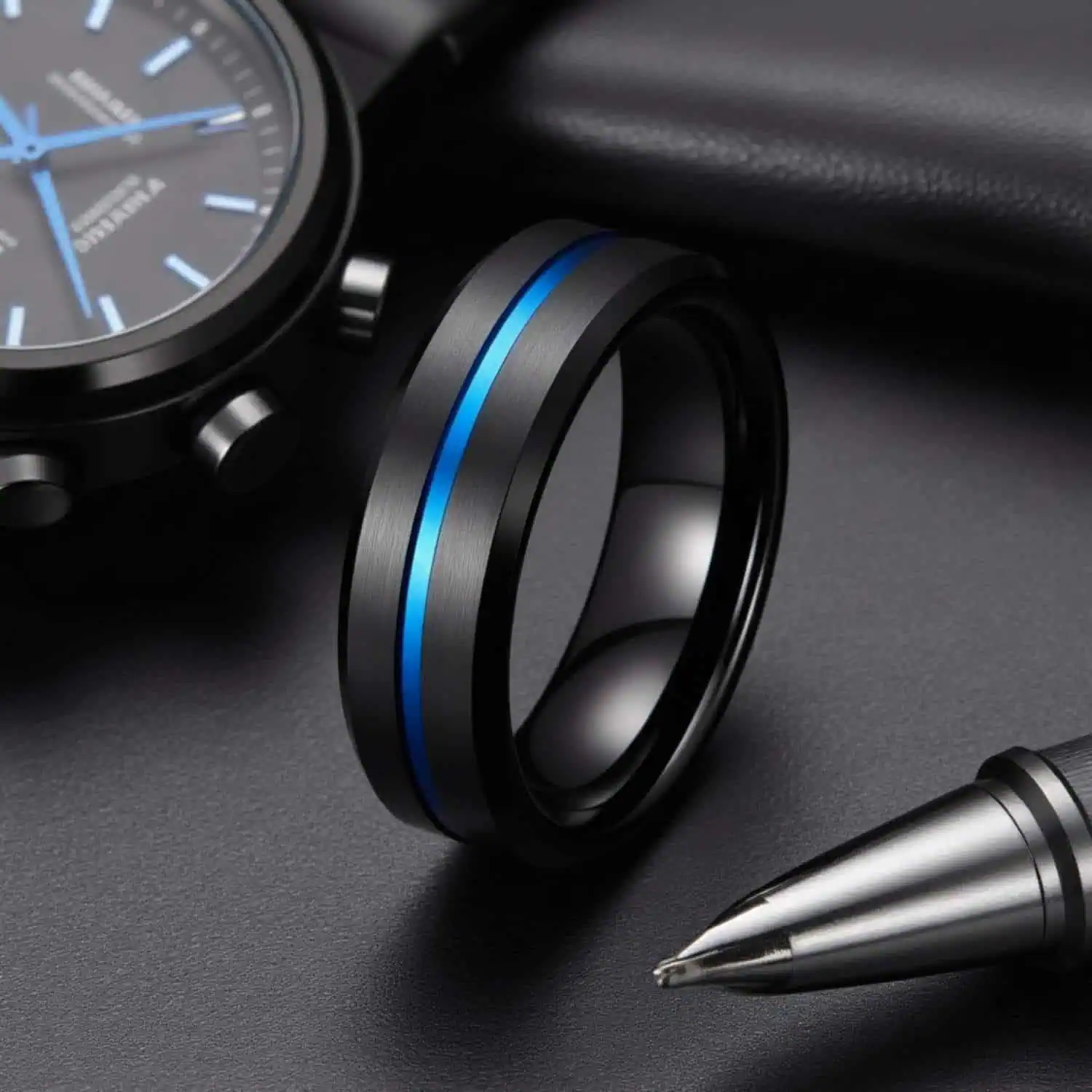 The Visionary men's tungsten ring standing upright beside a watch, leather case, and pen, highlighting its brushed black finish and polished blue centre groove.
