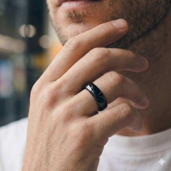 A close-up image of a man who has his hand held up to his chin. He is wearing a black tungsten ring that looks like a mans wedding ring. It is slightly domed in shape and is highly polished.