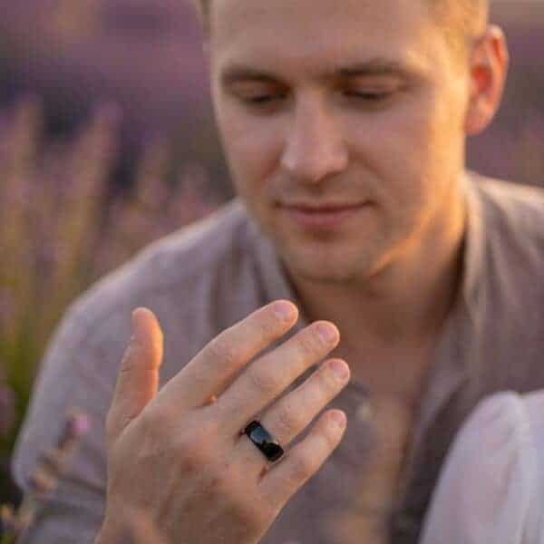 With a backdrop of lavender fields, a man faces the camera with his hand raised in front of him. He is wearing a polished black tungsten ring that is slightly domed in shape.