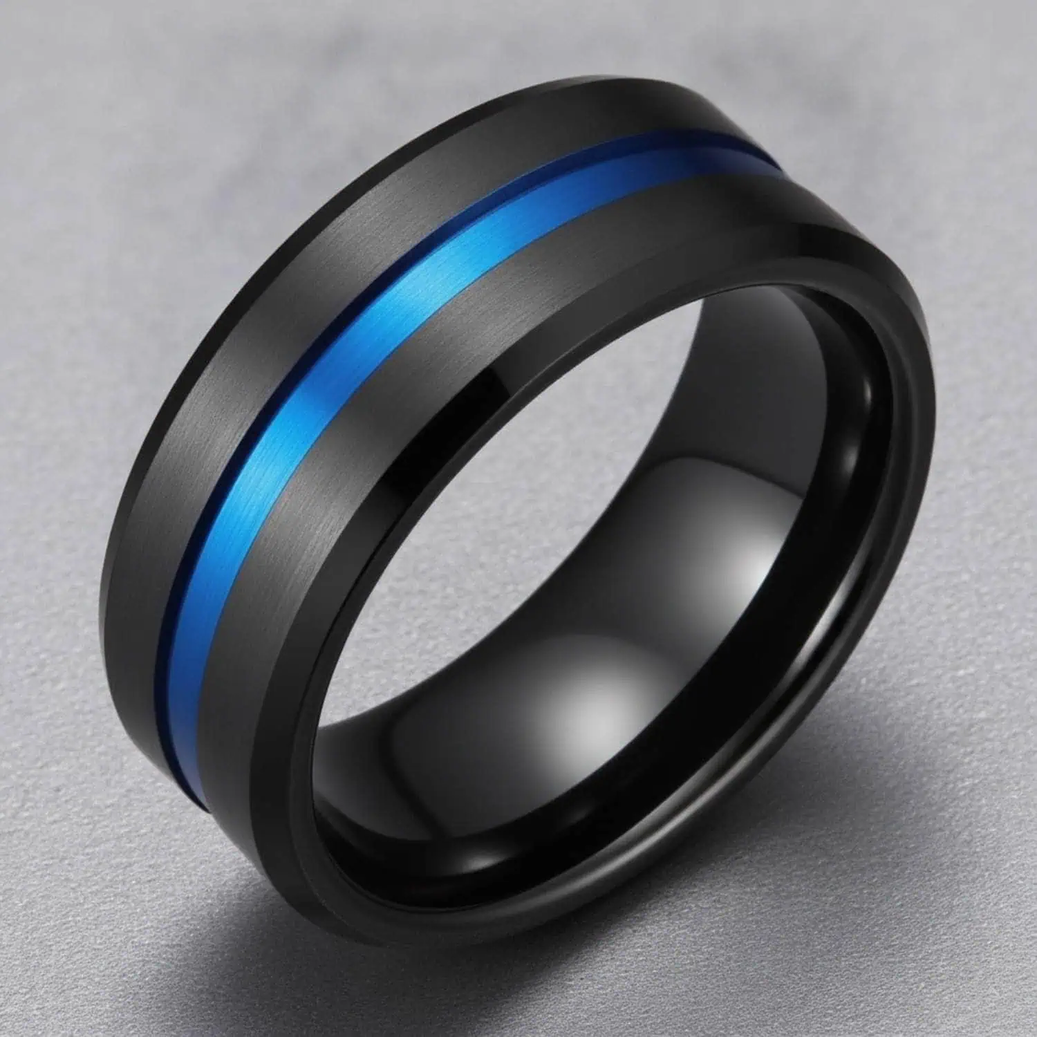 Studio close-up of the Visionary modern black tungsten ring against a plain grey background, featuring a brushed black surface, polished blue groove, and polished bevelled edges.
