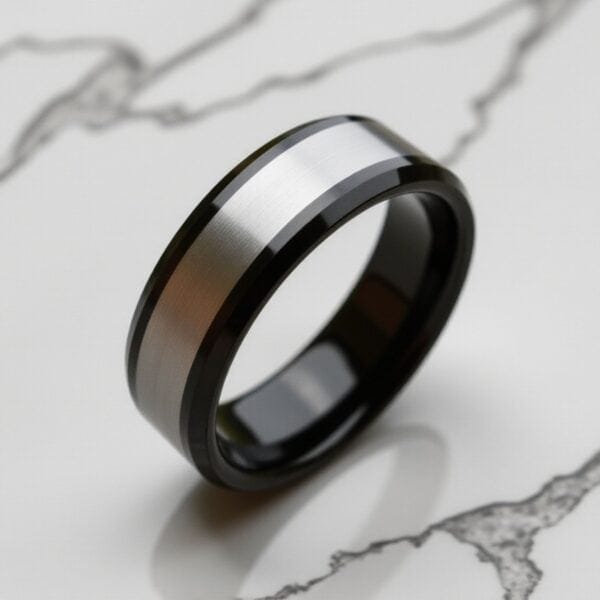 Standing upright on white marble is a silver and black tungsten ring. The inside of the ring is polished black.