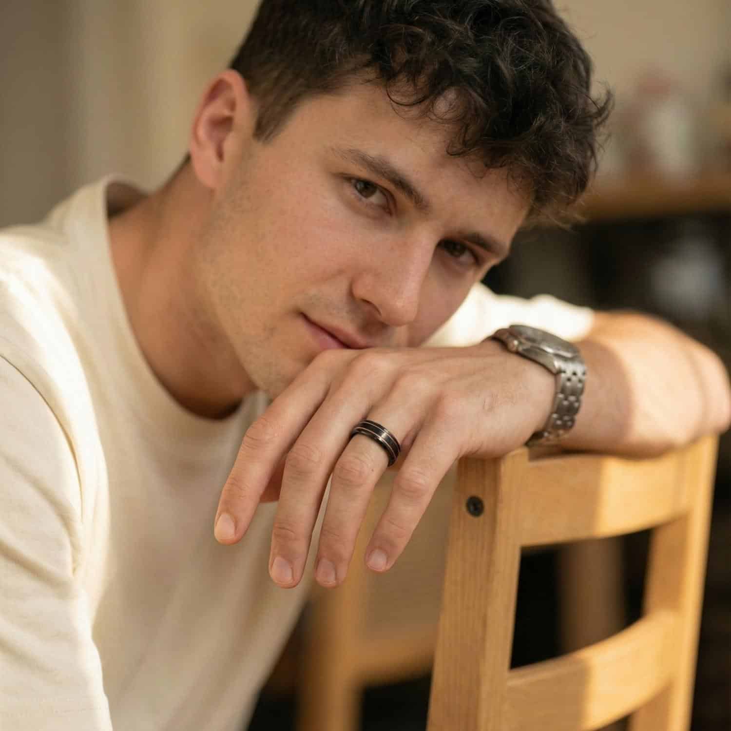 Leaning on the back of the chair in a relaxed pose, the man shows his black and gold tungsten ring.
