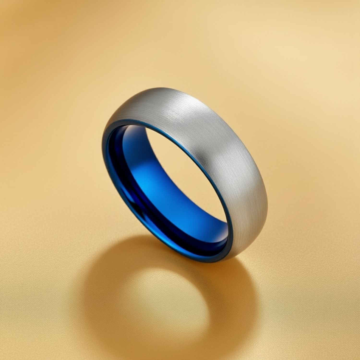 Set on a gold background, the image features a brushed silver tungsten ring, with a blue interior.