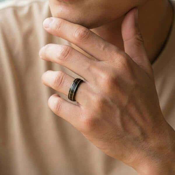 Bringing his hand to his chin in a thoughtful pose, the man is wearing a black tungsten ring which has two grooves of gold running through the ring.