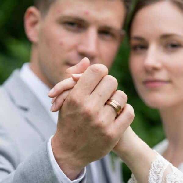 During the wedding ceremony, the couple reach their hands out towards the camera. The man is wearing a brown tungsten ring featuring a groove of rose gold. it has brushed and polished sections.
