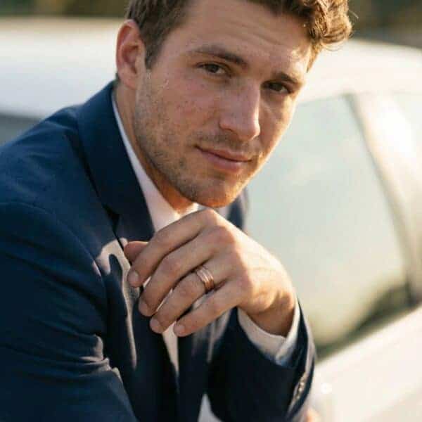 Dressed for work and ready for business, the man rests against his car. On his finger he wears a tungsten ring. It is a brown ring with a centre groove of rose gold. Featuring bevelled edges.