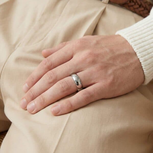 Resting his hand on his lap, the man is wearing a silver tungsten ring on his wedding finer. The ring is slightly domed and has a polished finish.