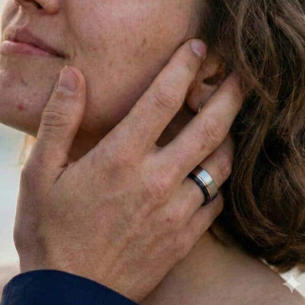 Cupping his partners face with his hands, the woman looks up towards him. On his hand, the man has a tungsten ring that is made up of a selection of colours - silver, rose gold, and black.