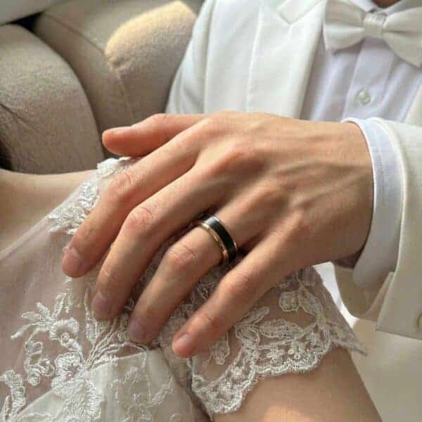 Just after the wedding ceremony, the bride and groom sit together. The man rests his hand on the brides shoulder. On his finger is his new wedding band. it is a black tungsten ring with rose gold edges.