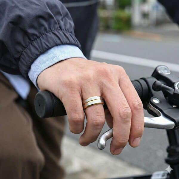 A close up of a man's hands holding onto the handlebars of his bike. On his hand is a mans gold and silver tungsten ring.