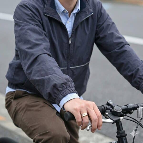 Riding on a bike, a man holds onto the handlebars. Wearing a raincoat, the man has a gold and silver tungsten ring on his hand.