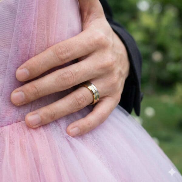 A couple embrace, the mans hand around his partners waist. She is wearing a pink dress. The man is wearing a gold and silver tungsten ring with bevelled edges.