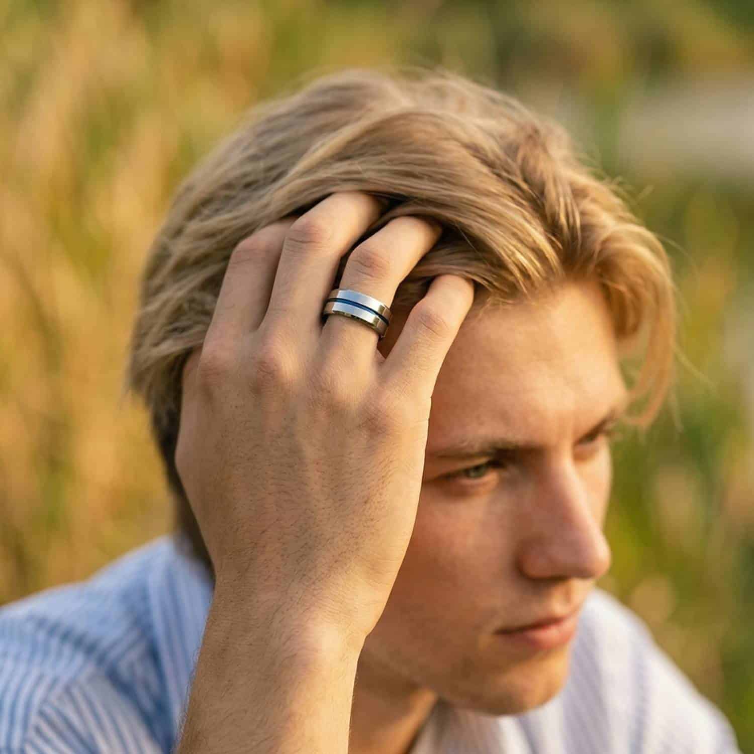 Man in striped shirt in thoughtful pose wearing polished silver tungsten ring with blue groove, green grass background