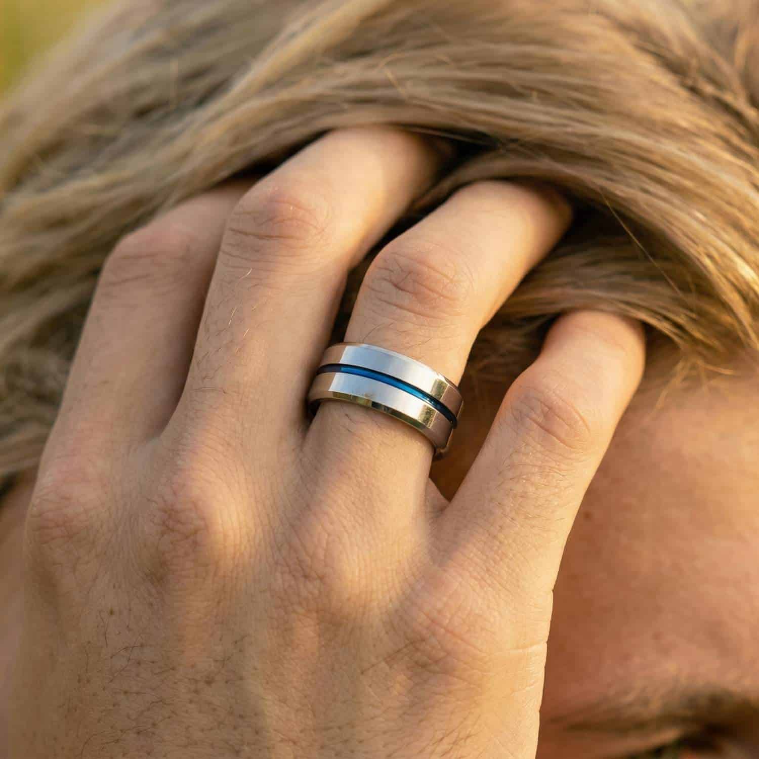 Close-up of man’s hand running through hair wearing polished silver tungsten ring with blue groove