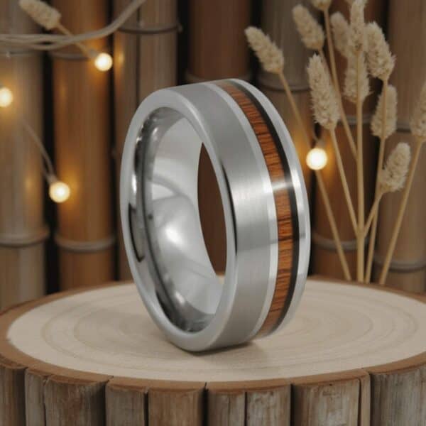 A lovely natural setting, set against a fence made with bamboo and with fairy lights shimmering, a tungsten ring sits on a wooden stand. The silver tungsten ring has an inlay of natural wood.