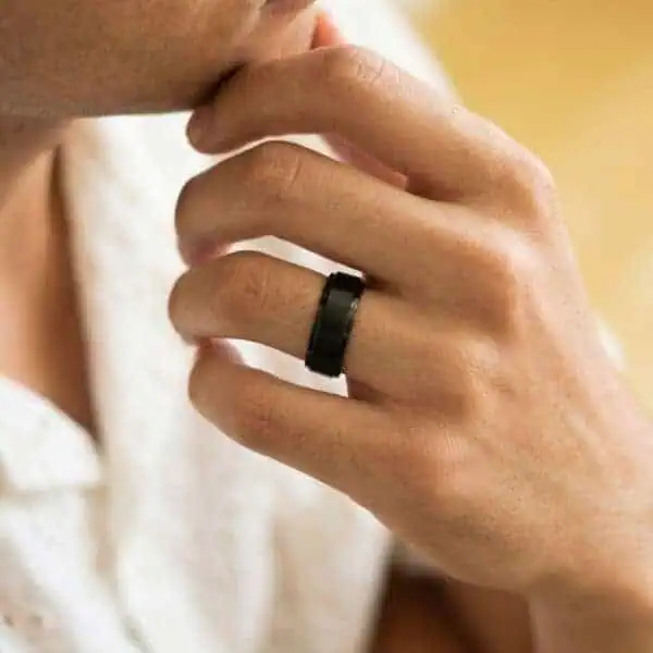 A close up image of a hand resting on a mans chin. He is wearing a black ring on his wedding finger. The ring is made with tungsten. It has a brushed centre and polished edges.