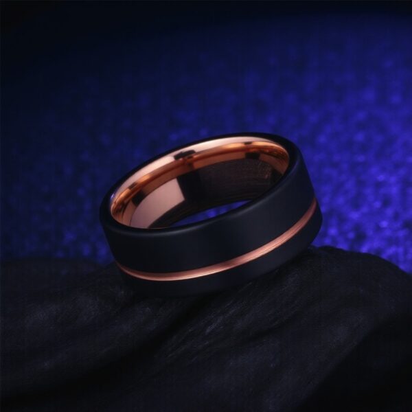 With a futuristic background, a ring lays sideways. The feature of the image, the ring is black with rose gold. Made with tungsten, the groove and inside of the ring are polished rose gold.