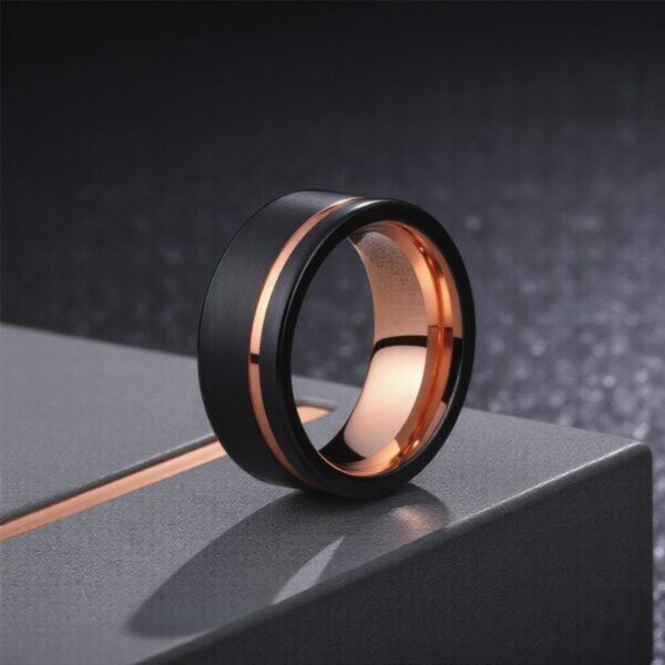 Standing upright on the grey stand is a black and rose gold tungsten ring. The ring is brushed black with a stripe of rose gold running through it. The inside of the ring is also rose gold.