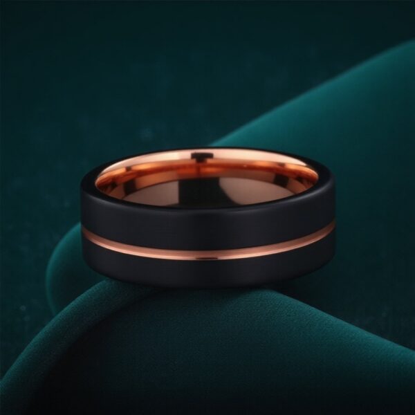 On dark green velvet, this black and rose gold ring lays on its side. Featuring a rose gold groove, and a rose gold inside, this is a brushed black tungsten ring.