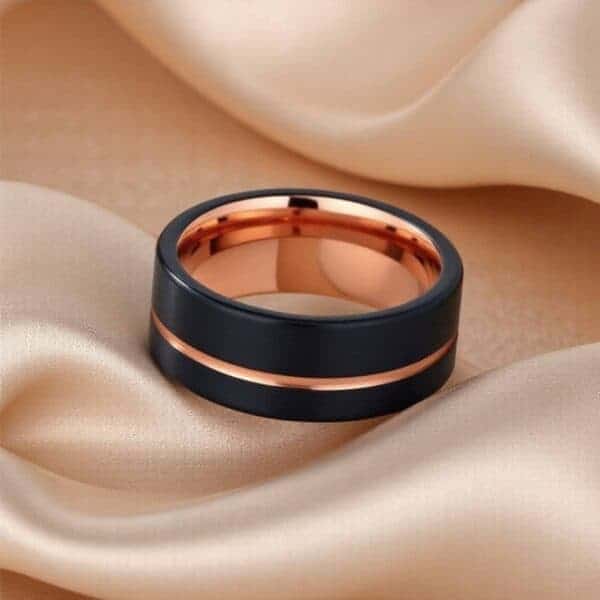 On luxurious silk, a ring lays on its side. This black and rose gold ring is made with tungsten. The black has a brushed finish and the rose gold is polished.
