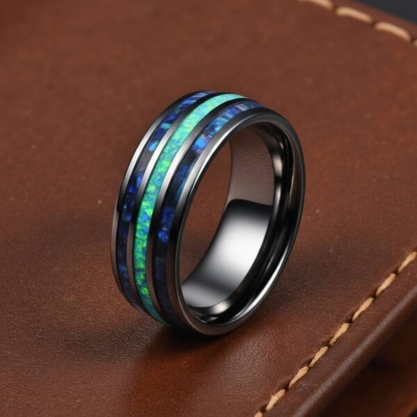A ring stands upright on a brown leather book. The ring is a silver tungsten ring that features a central inlay of turquoise and two inlays of abalone shell on either side of the turquoise.