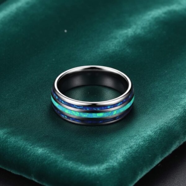 A silver tungsten ring lays flat on a green velvet box. The silver ring features inlays of turquoise and abalone shell.