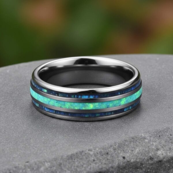 In an outdoor setting, a ring has been placed flat on a stone. The silver ring has a vibrant turquoise section at its centre and two abalone sections on either side.