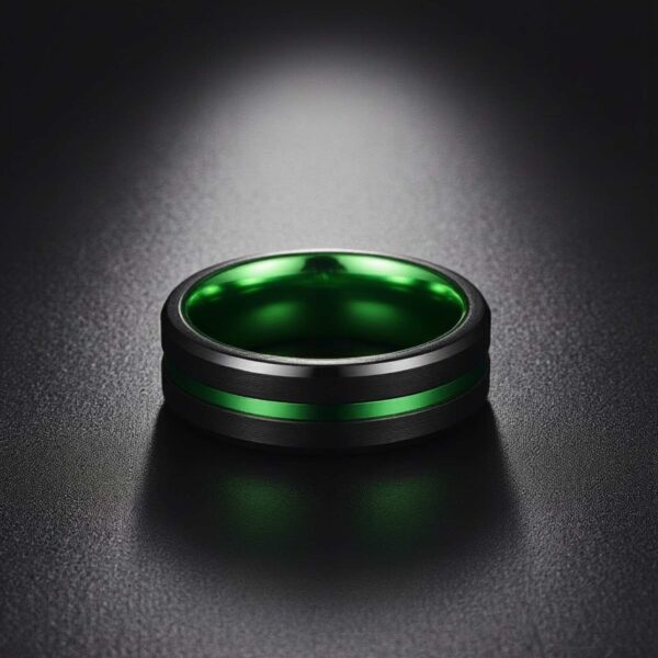 A black tungsten ring sits on a leather surface with a spotlight shining down on it. The ring features a groove of green and a green inside.