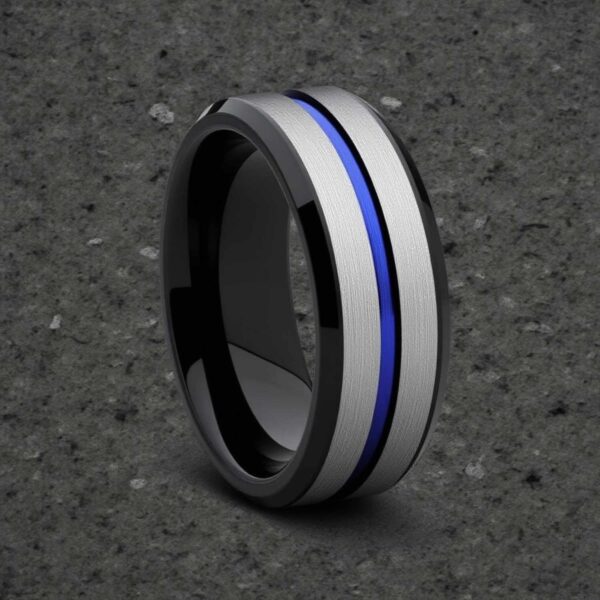 On a minimalist grey background, a ring stands upright. It is a tungsten ring featuring silver, blue and black. With a mix of brushed and polished finishes.
