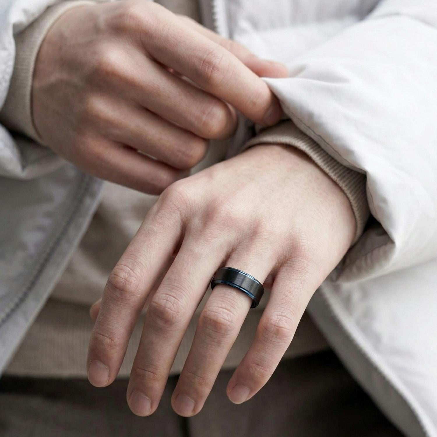 A close up image of a man's hands. Wearing a white jacket, he has a black tungsten ring on his wedding finger. The ring has contrasting blue edges.