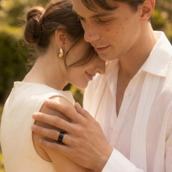 During the wedding ceremony, the couple share a quiet moment together. The bride, dressed in her wedding gown, stands next to the groom who is wearing a white shirt. On his finger, he wears a black tungsten ring. The ring has raised brushed sections and a smooth groove that runs through the centre of the ring.