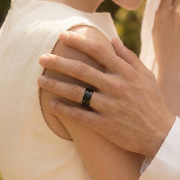 A close up of the newly married couple as they hold each other. The mans hand is visible. He is wearing a black tungsten ring.