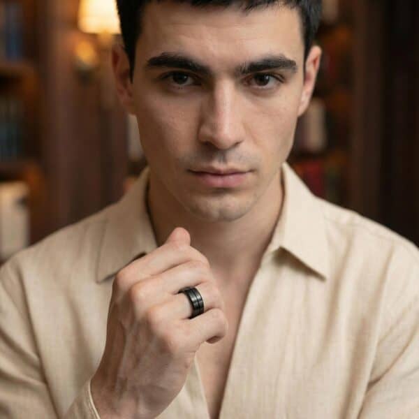 Facing the camera and with his hand held up in front of him, the man is wearing a cream shirt. On his hand, he wears a black tungsten ring.