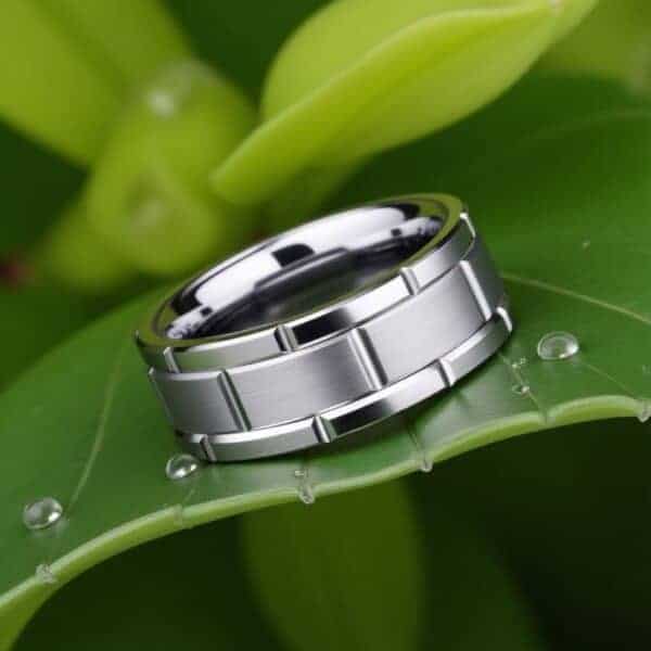 Resting on a bright and vibrant green leaf lays a silver ring. The band is made with tungsten and features a distinctive block pattern.