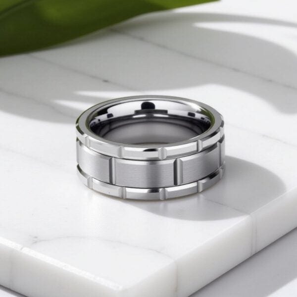 On white marble, there is a close up shot of a silver tungsten ring. The ring has a brickwork pattern that makes for a unique mans band.