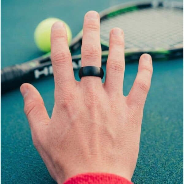 Tennis racquet down, the tennis player stretches out his hand. He is wearing a black tungsten ring that has a light brushed finish. The ring is slightly domed in shape.