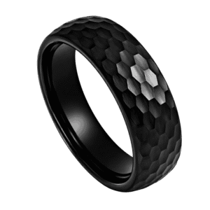 A close up image of a mans black ring. Made with tungsten, this black ring has a hammered effect finish. This means that the ring catches the light from many different angles.