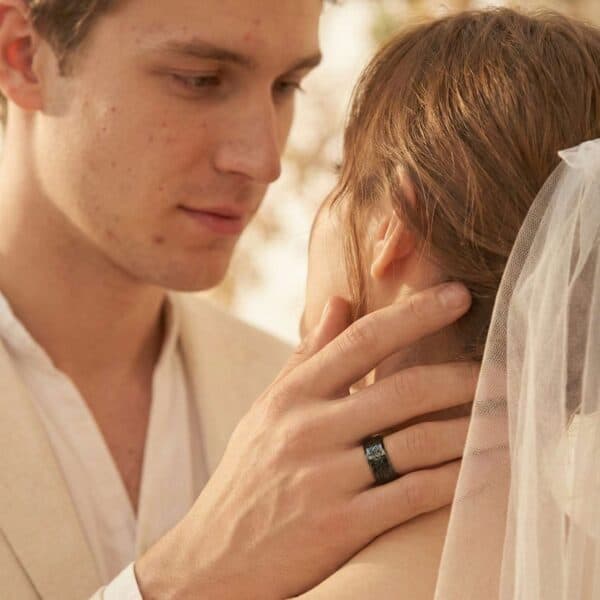 The wedding couple are about to kiss. Tenderly holding the bride, the man is wearing his wedding ring. It is a black tungsten ring that features a inlay of black faux meteorite.