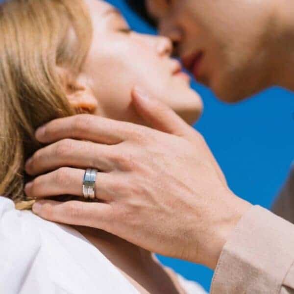 A couple come together for a kiss. The man has his hand held to the womans face. He is wearing a silver tungsten ring that has brushed sections and a polished silver groove.