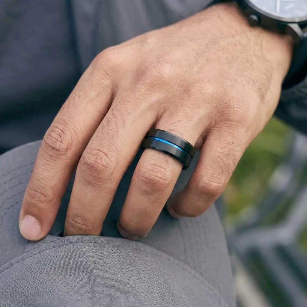 Close-up of a man's hand wearing the Unswerving black titanium ring featuring a polished blue groove, blue interior, and bevelled edges.