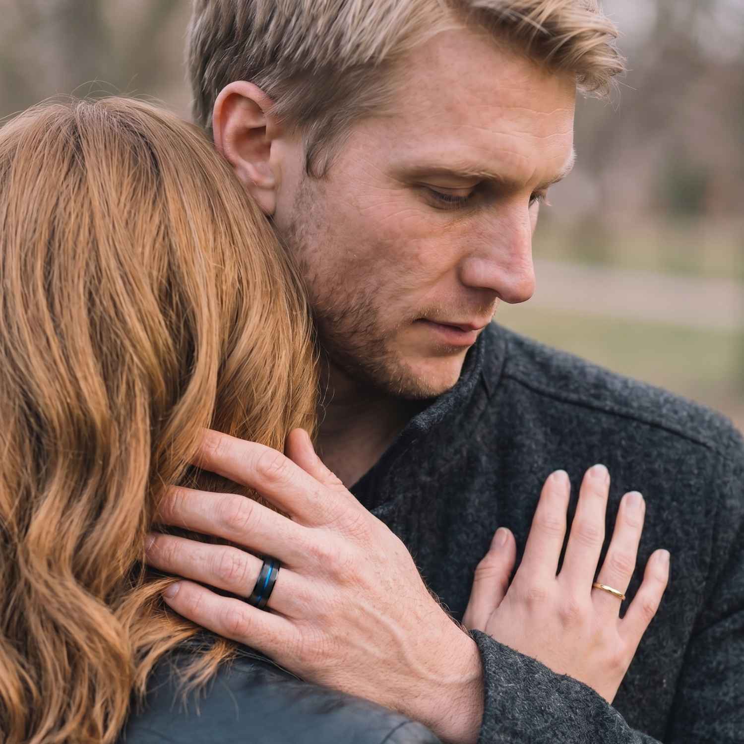 Couple embracing with the man wearing the Unswerving black titanium men's wedding band with a polished blue groove as his hand rests on his partner's shoulder.